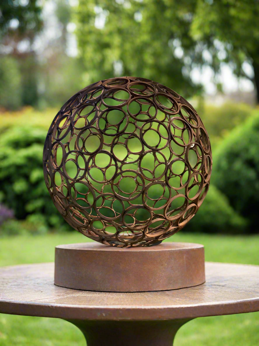 Smaller version of rustic garden sphere sculpture in weathered steel, displayed on a round pedestal, ideal for garden tables or patio decor.