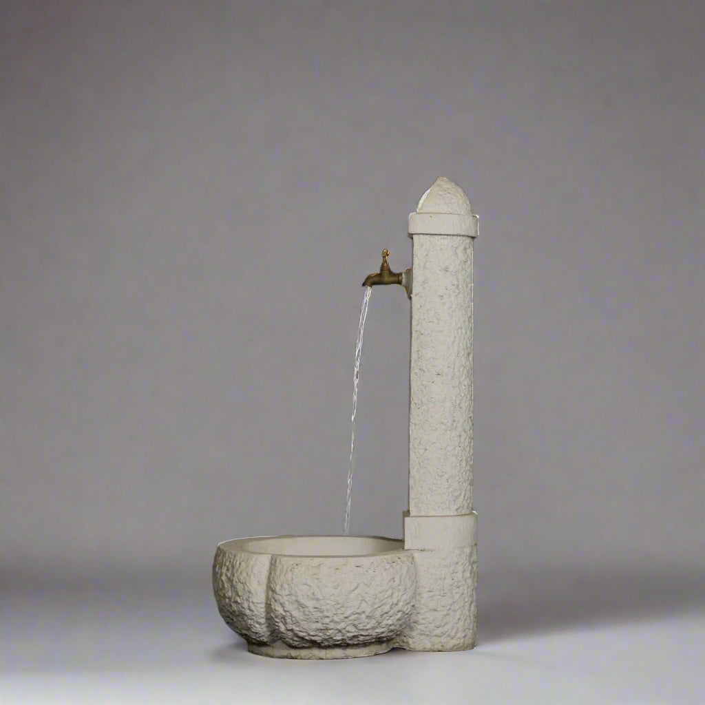 Large Stone Fountain with rustic textured finish and curved base, water streaming from brass tap, suitable for outdoor garden settings.