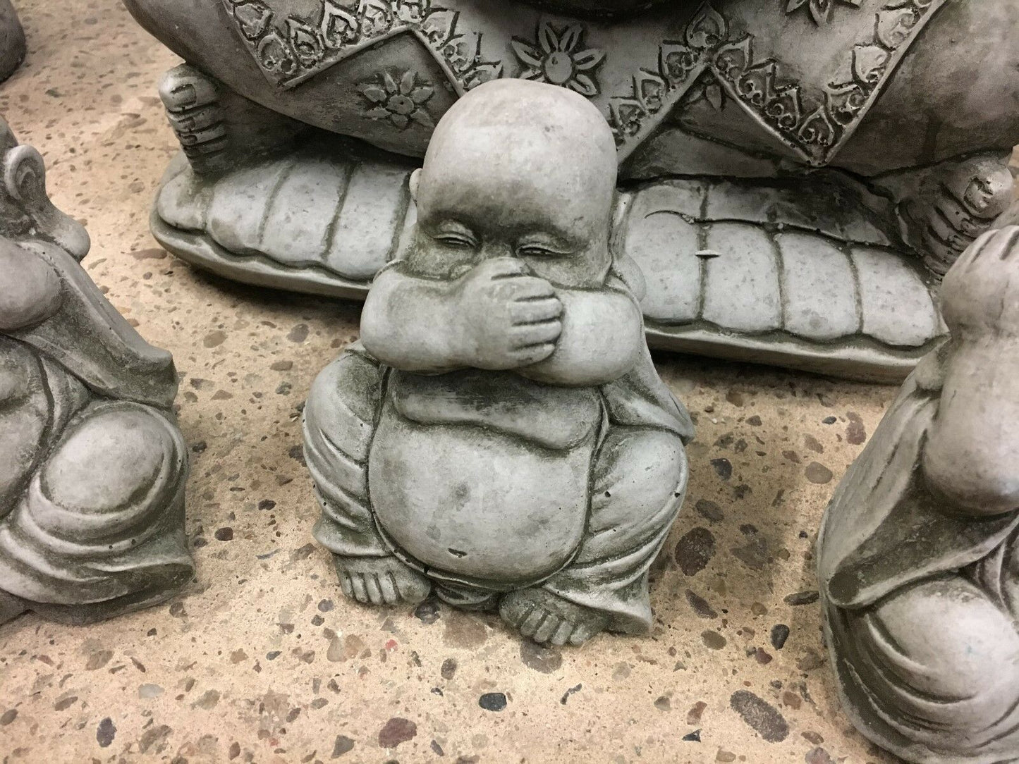 Zoomed-in 'Speak No Evil' Buddha statue with hands over mouth, part of a decorative stone garden ornament trio.