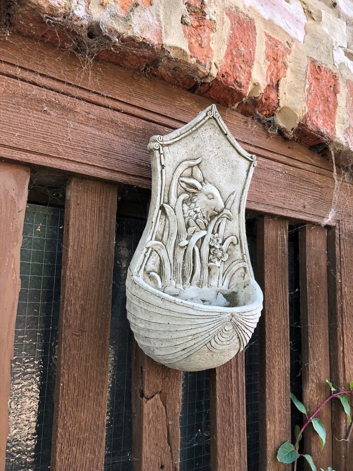 Antique grey Stone Rabbit Planter with drainage hole, mounted on rustic wood, perfect for garden or patio wall decoration.