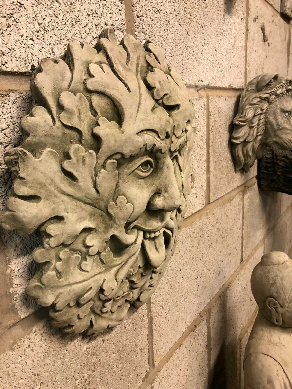Side view of Stone Tongue Out Greenman Plaque mounted on wall, highlighting 3D sculptural depth and intricate leaf detailing for outdoor decor.