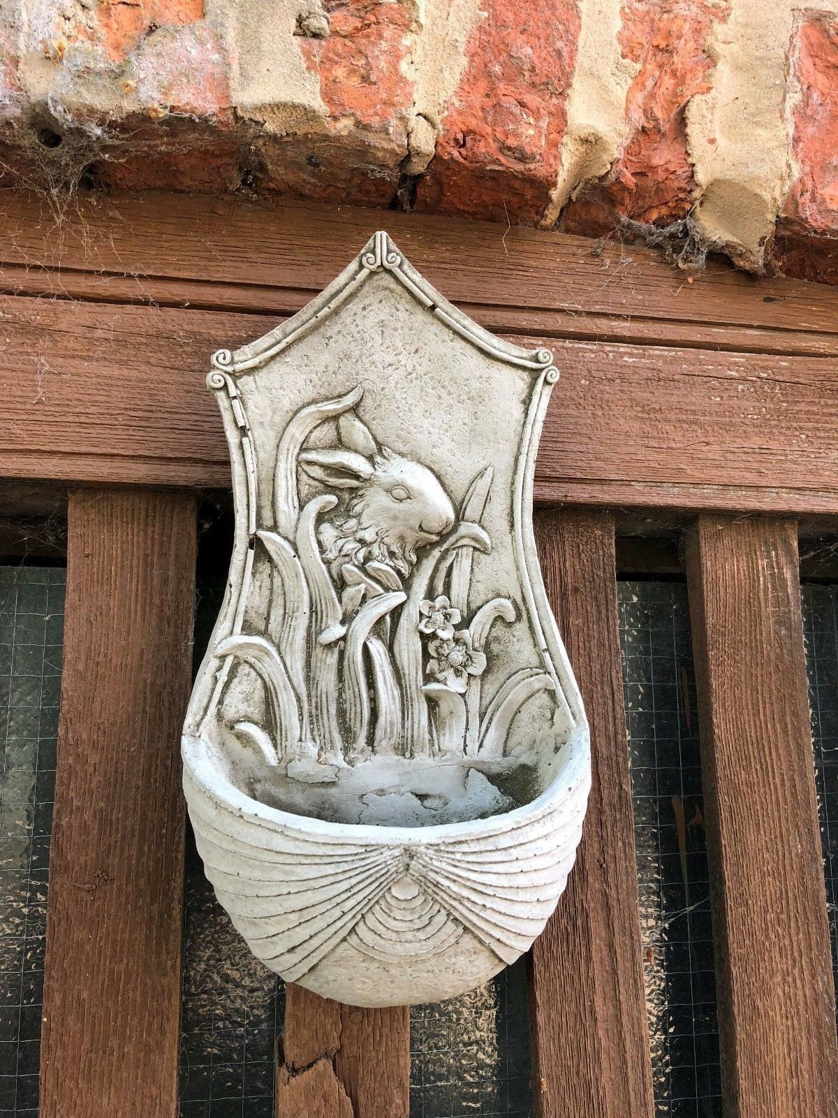 Front view of Stone Rabbit Planter mounted on wooden wall, featuring intricate bunny and flower relief in antique stone finish.