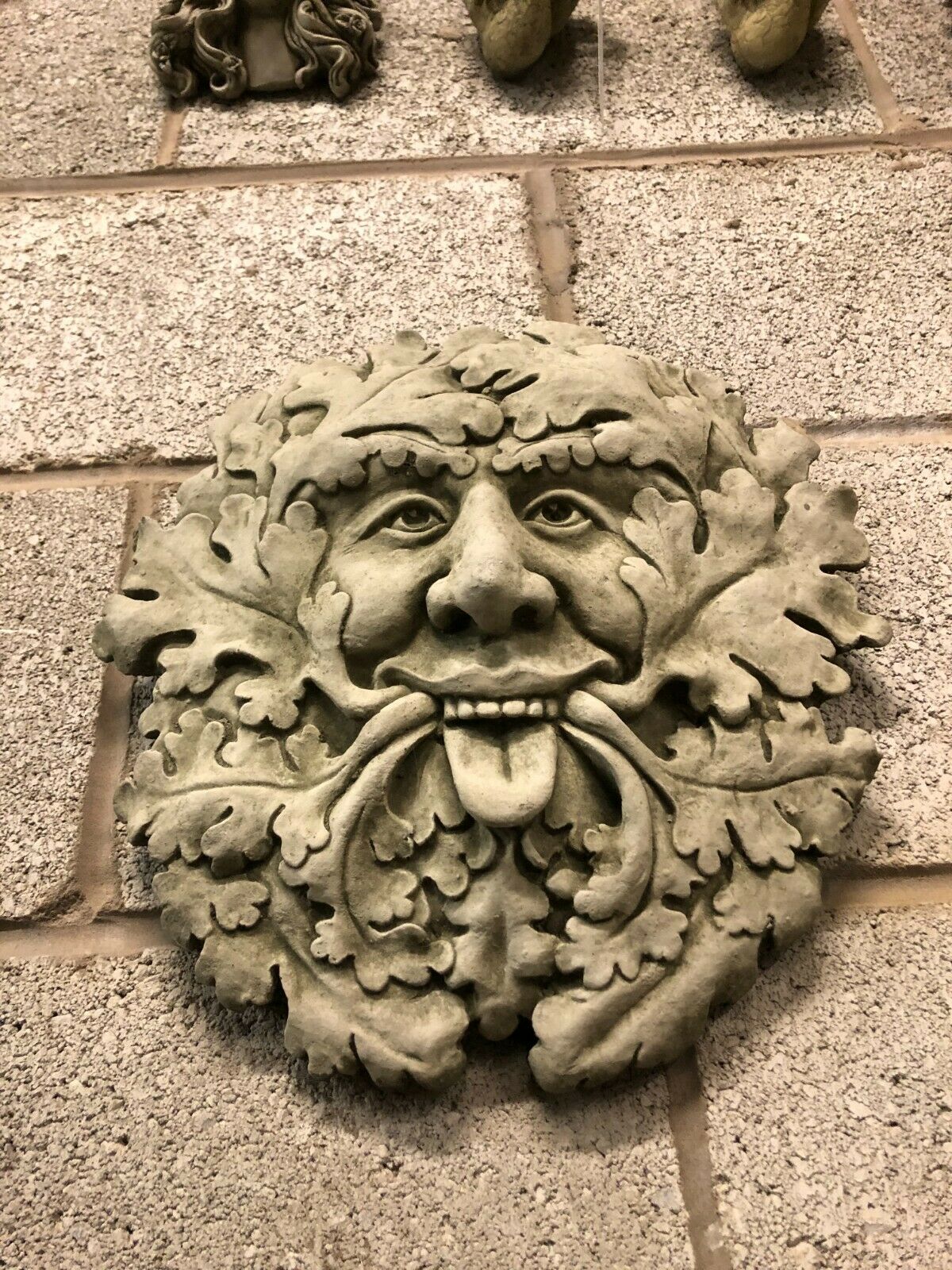 Front view of Stone Tongue Out Greenman Plaque with whimsical expression and durable limestone finish, great for decorative wall mounting.