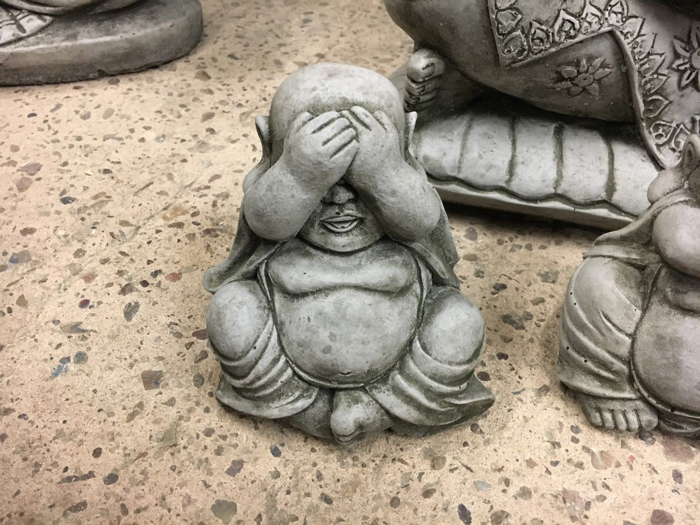 Close-up of 'See No Evil' Buddha ornament with hands covering eyes, crafted from durable stone for outdoor garden decoration.