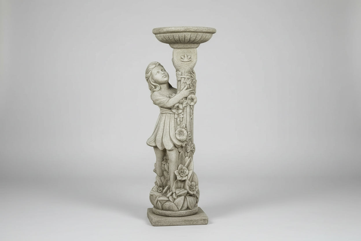 Decorative stone statue of a woman holding a bird bath in a garden with pink and red flowers.