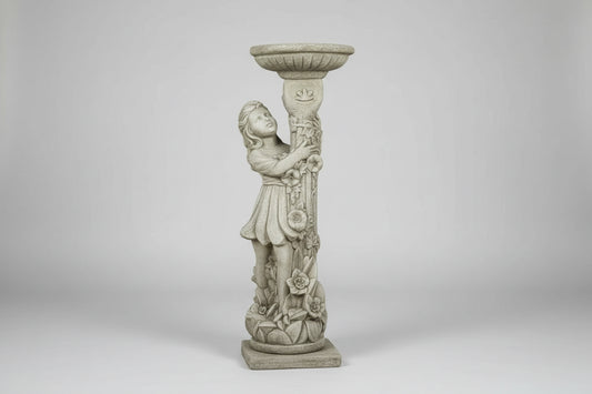 Decorative stone statue of a woman holding a bird bath in a garden with pink and red flowers.